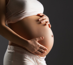 Pregnant woman holding her belly over gray background